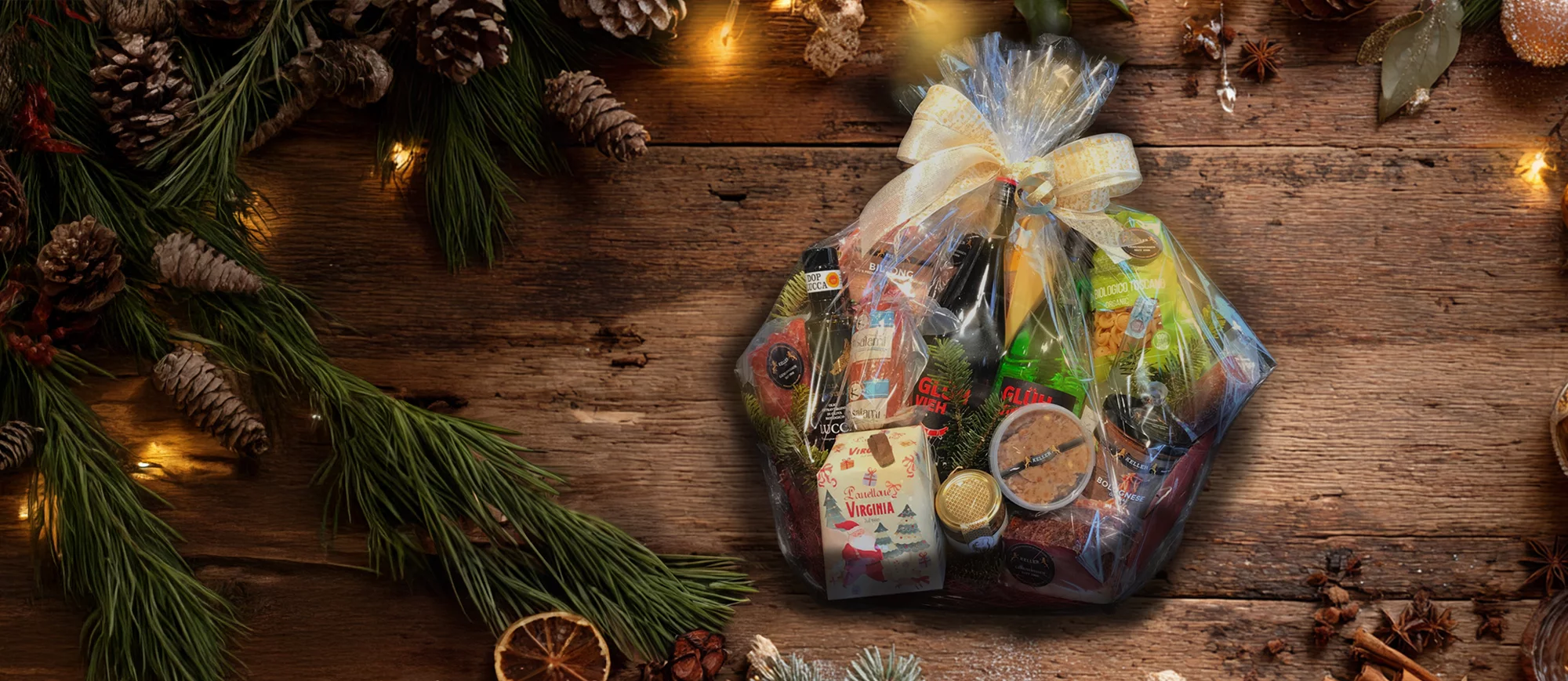 Ein eingepackter Geschenkkorb mit Feinkostspezialitäten auf einem weihnachtlich geschmückten Holztisch